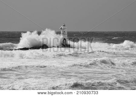 White lighthouse on the cliff. Lighthouse Mangiabarche located in the south of Sardinia. Italy. Black and white, gray sky, white wave.