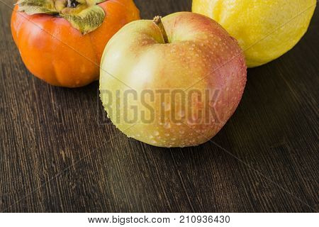 apple persimmon and lemon on a wooden brown table