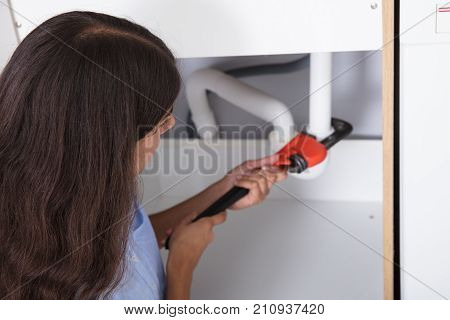 Close-up Of Young Woman Tightening Sink Pipe With Monkey Wrench In Kitchen