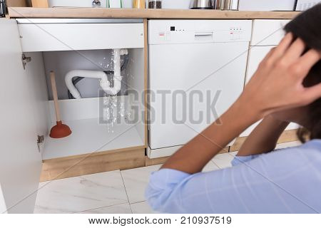 Troubled Woman Looking At Leaking Sink Pipe In Kitchen