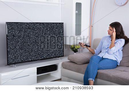 Rear View Of A Woman On Sofa Getting Frustrated With Glitch TV Screen At Home