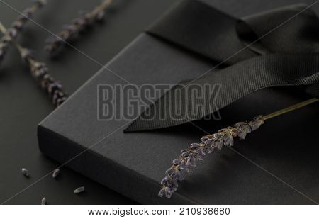 Black gift box on a dark contrasted background decorated with a textured bow and lavender creating a romantic atmosphere. Typically used for birthday anniversary presents gift cards post cards letters.