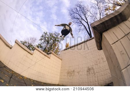A Young Guy Performs A Jump Through The Space Between The Concrete Parapets. The Athlete Practices P