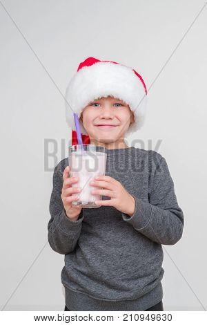 Little blond emotional boy in a festive red hat in a gray sweater with milk