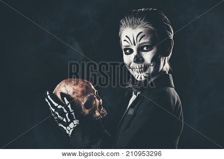 Portrait of a child boy with carnival make-up of a skeleton wearing elegant tail-coat. Studio shot over black background. Halloween. Dia de los muertos. The Day of the Dead.