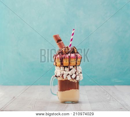 Chocolate and donuts extreme milkshake with marshmallow and other sweets in mason jar on gray wooden table and blue background. Crazy freakshake on gray and blue background with copy space