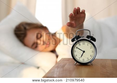 Sleepy young woman stretching hand to ringing alarm willing turn it off. Early wake up, not getting enough sleep, getting work concept