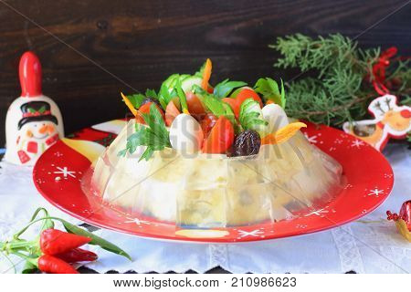 Traditional Russian meat salad with a jelly cubes coat decorated with quail eggs cherry tomatoes cucumbers paprika olives and parsley on a Chrismas traditional plate