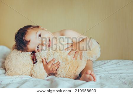 cute baby boy with teddy bear in bedroom. Newborn child smiling and relaxing in bed. Nursery for young children. Family morning at home.