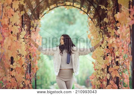 Autumn girl playing in city park. Fall woman portrait of happy lovely and beautiful mixed race Asian Caucasian young woman in garden arch in fall colors. Model in white casual clothes looking smiling toching leaves and looking at nature beauty.