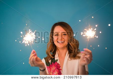 Happy woman having fun with a sparkler on blue background with copyspace.