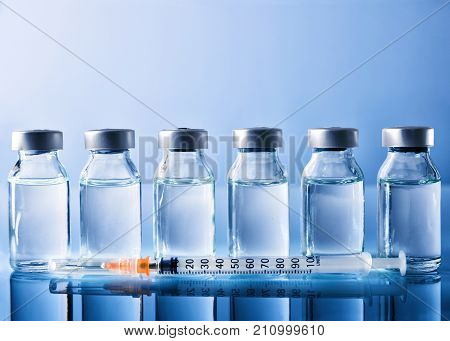 Row Of Vials And Syringe On Blue Table Front View