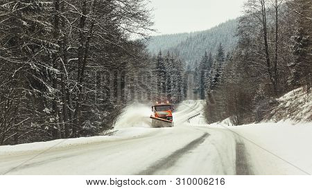 Bright Orange Plough Truck Cleaning Snow On Forest Road In Winter, View From Car Driving Other Way, 
