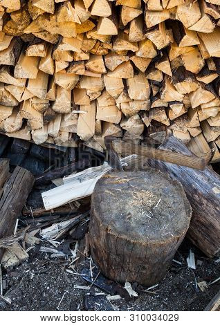 Axe In A Stump Near The Stack Of Chopped Firewood Logs. Wood Splitting. Close-up.