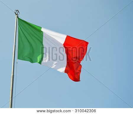 Italian National Flag Vawing In The Wind With Blue Sky Used As Background