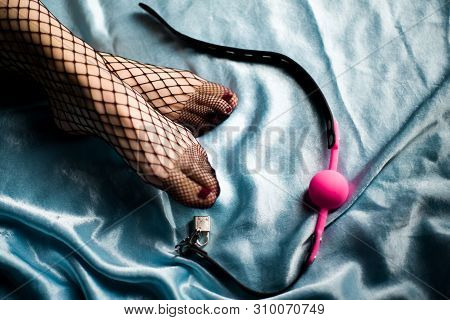 Pink Gag Ball Lies On A Blue Satin Next To The Beautiful Female Legs In Stockings In A Fishnet. Bdsm