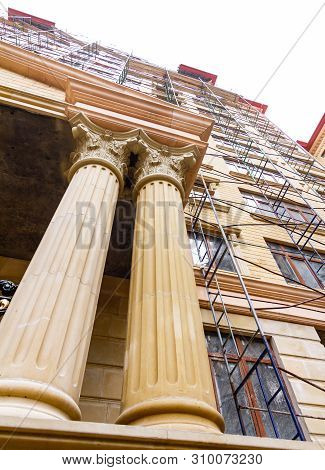 Columns Adorning The Entrance To A Multistory Building Under Construction. Scaffolding To The Top Fl