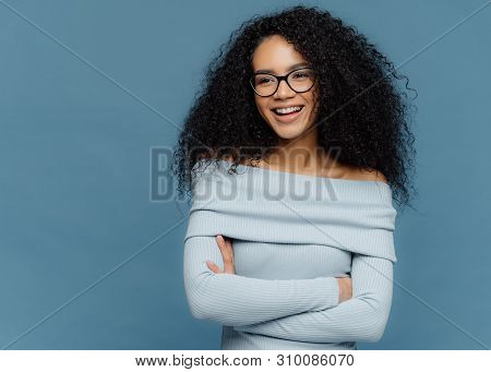 Cheerful Female Student Has Perfect Mood, Curly Bushy Hair, Arms Folded, Looks Somewhere With Positi