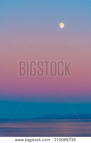 Moon With Pink Skies At Blue Hour Twilight Before Sunrise/ Following Sunset Over Ocean With Reflecti