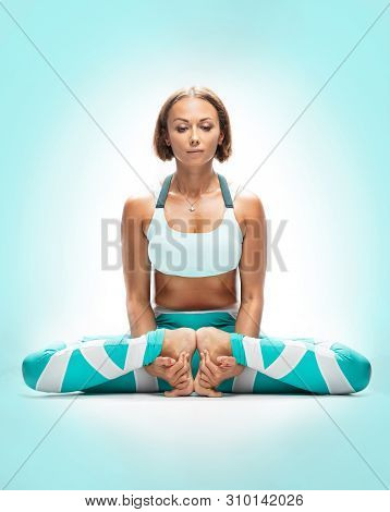 Athletic Young Woman Practicing Yoga On Turquoise Background. Mulabandhasana.