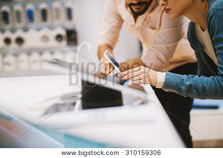 Young Indecisive Couple Checking Out Mobile Phones In The Mobile Store.