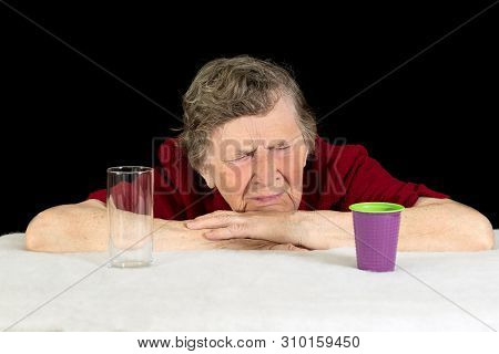 An Elderly Woman With Gray Hair And Wrinkles On Her Face Looks At The Disposable Plastic Cup With Di