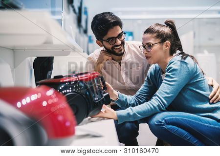 Young Lovely Husband And Wife Deciding Which Vacuum Cleaner To Buy In The Electronic Store.