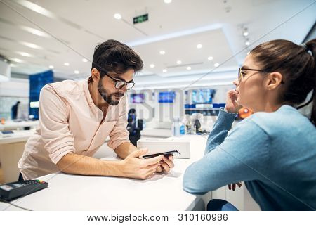 Cute Young Modern Girl Talking With Tech Shop Employe About The Mobile Phone.