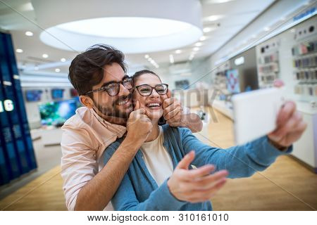 Lovely Cheerful Hipster Couple In The Tech Store Taking A Selfie With The Shop Phone.