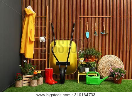 Gardening Tools With Wheelbarrow And Flowers Near Wooden Wall