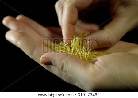 Close-up Of Human Fingers Touches Handful Of Vermicell In Hand On A Black Background, Unrecognizable