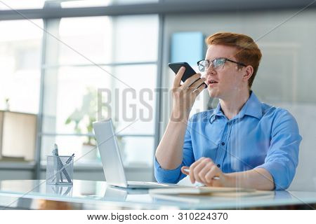 Young creative employee recording voice message in office