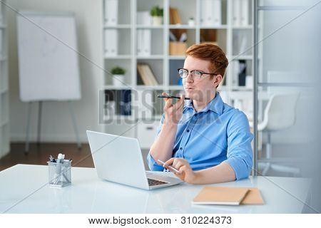 Young elegant businessman recording voice message by workplace