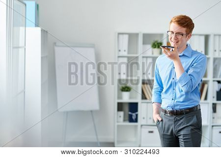 Handsome young businessman recording his voice on dictophone