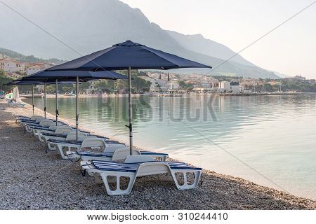 Parasols And Deck Chairs On The Beach In Baska Voda, Croatia
