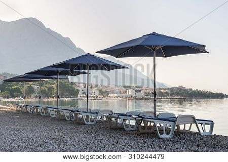 Parasols And Deck Chairs On The Beach In Baska Voda, Croatia