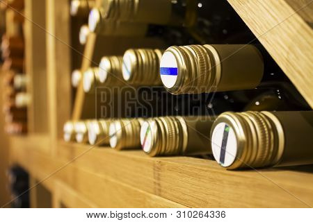 Bottles Of White Wine With Golden Colored Wrap Laying Down On The Wooden Shelf In Dark,fresh Cellar