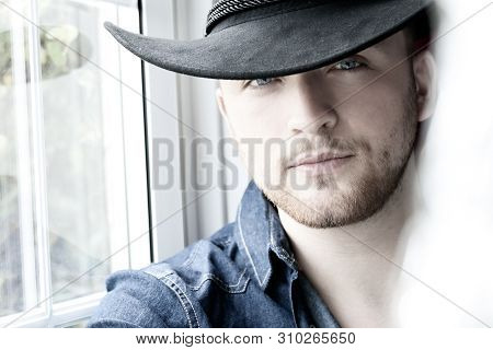 Portrait Of Hot Male Cowboy Wearing Hat Sitting In Window