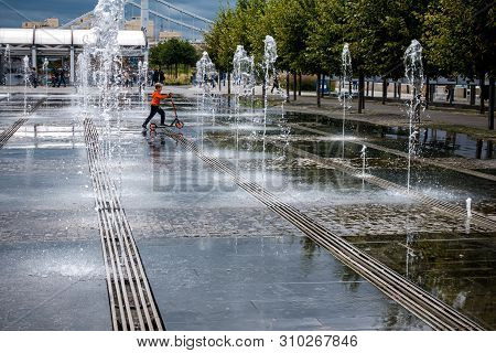 Moscow,museon Park,september 4,2016: Boy Fun Riding A Scooter Between The Jets Of Water In The Fount