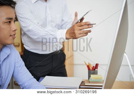 Entrepreneur Pointing At Computer Screen When Explaining Work To New Emplyee