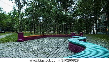 Slightly Blurred Image Of An Empty Bench In The Small Square Near The Appartaments In The Dark Eveni