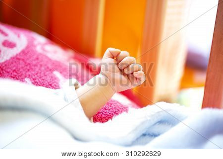 Hand Of An Energetic Newborn Baby With Light Blue And Pink Blanket And Baby Bed. Close Up.