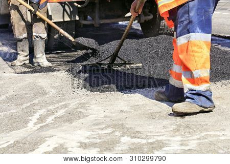 The Group Of Road Workers Renews A Section Of The Road With Fresh Hot Asphalt Using A Spade And Wood