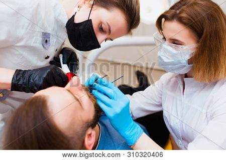 Dental Clinic. Professional Doctor Dentist Treats Teeth To The Patient In The Office On Modern Equip
