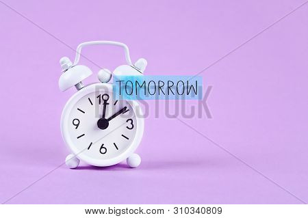 Procrastination, Delay And Urgency Concept. White Alarm Clock With A Sticky Note With Text Tomorrow