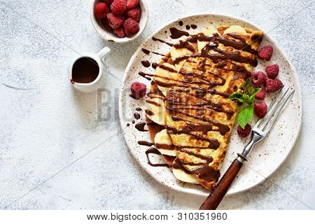 Crepe With Chocolate Paste, Banana And Raspberries On A Concrete Background. Tasty Breakfast.