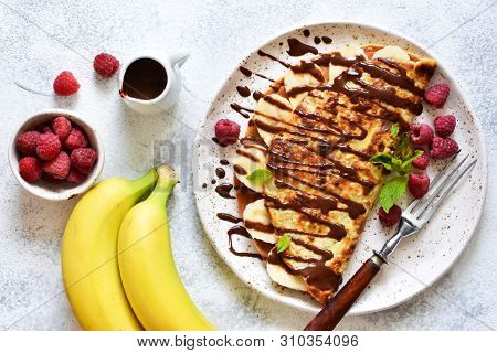 Crepe With Chocolate Paste, Banana And Raspberries On A Concrete Background. Tasty Breakfast.