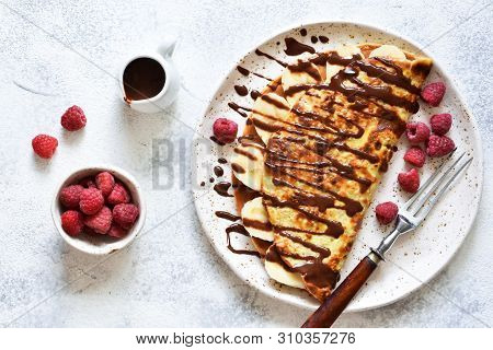 Crepe With Chocolate Paste, Banana And Raspberries On A Concrete Background. Tasty Breakfast.