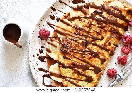 Crepe With Chocolate Paste, Banana And Raspberries On A Concrete Background. Tasty Breakfast.