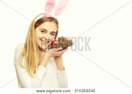 Happy Easter Girl In Pink Bunny Ears With Red Painted Egg In Straw Nest, Has Long Blonde Hair And Sm